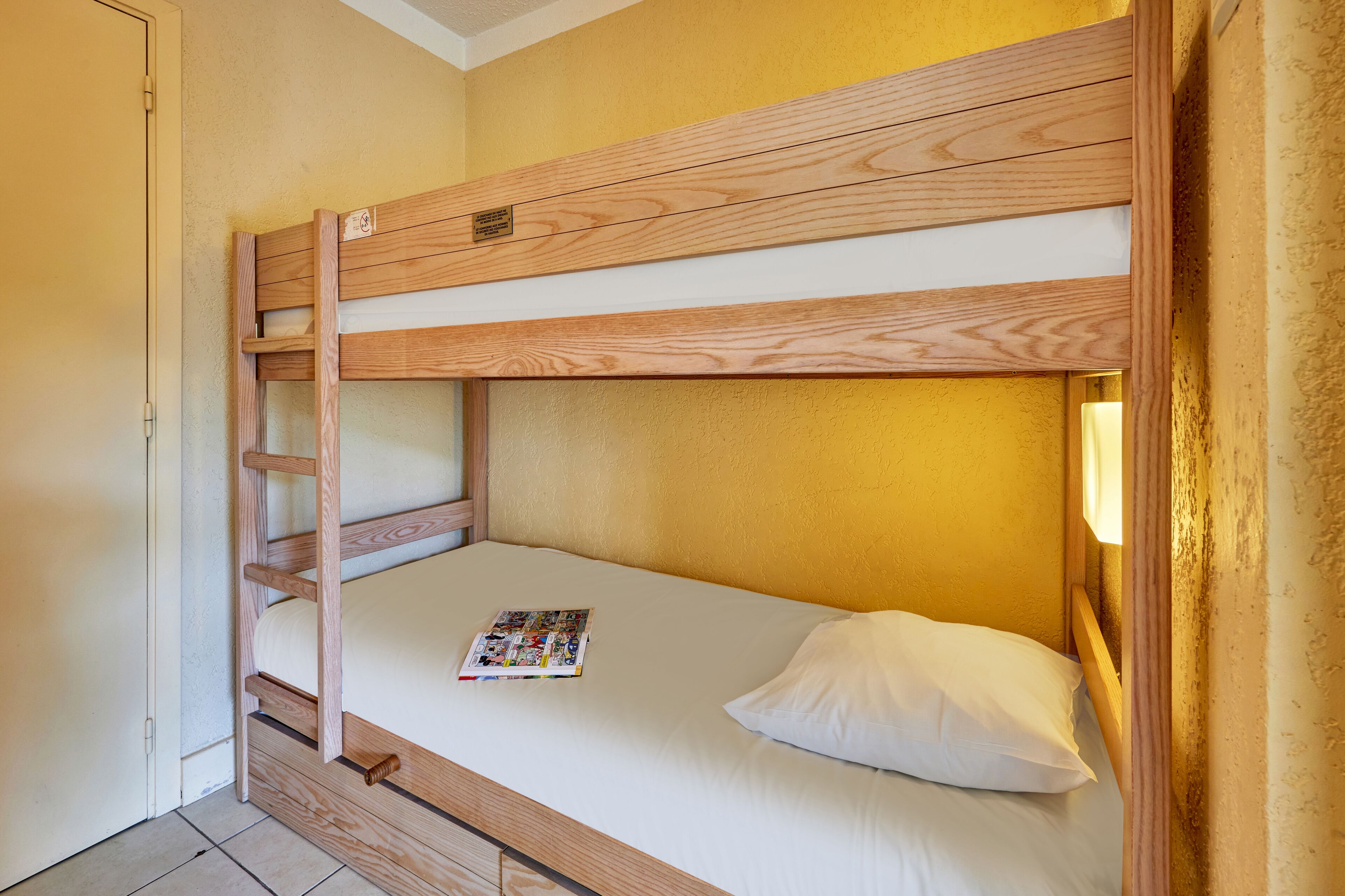 Een stapelbed met houten frame, een ladder en een tijdschrift op de matras.