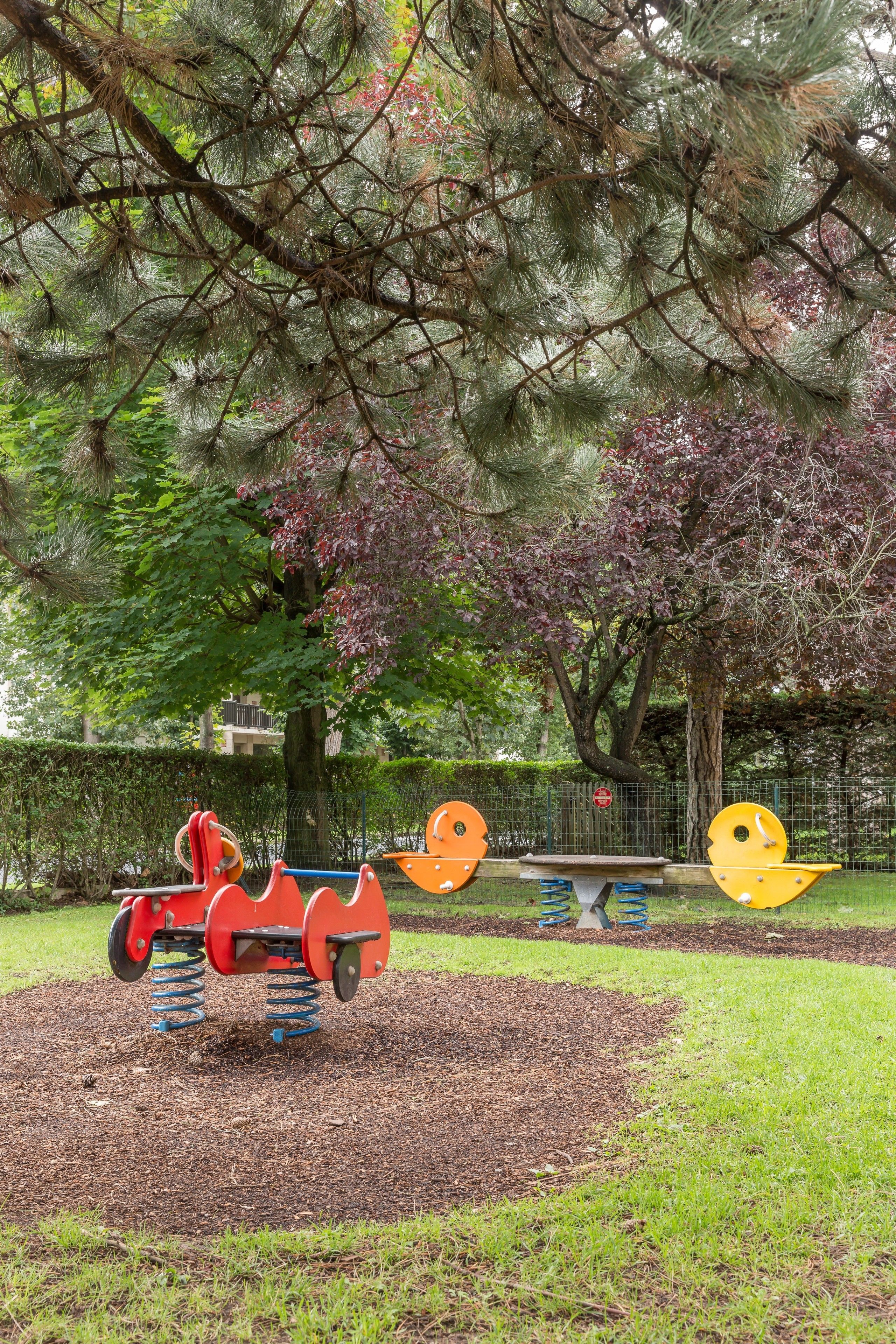 A playground with swings and a slide, surrounded by trees and a fence.