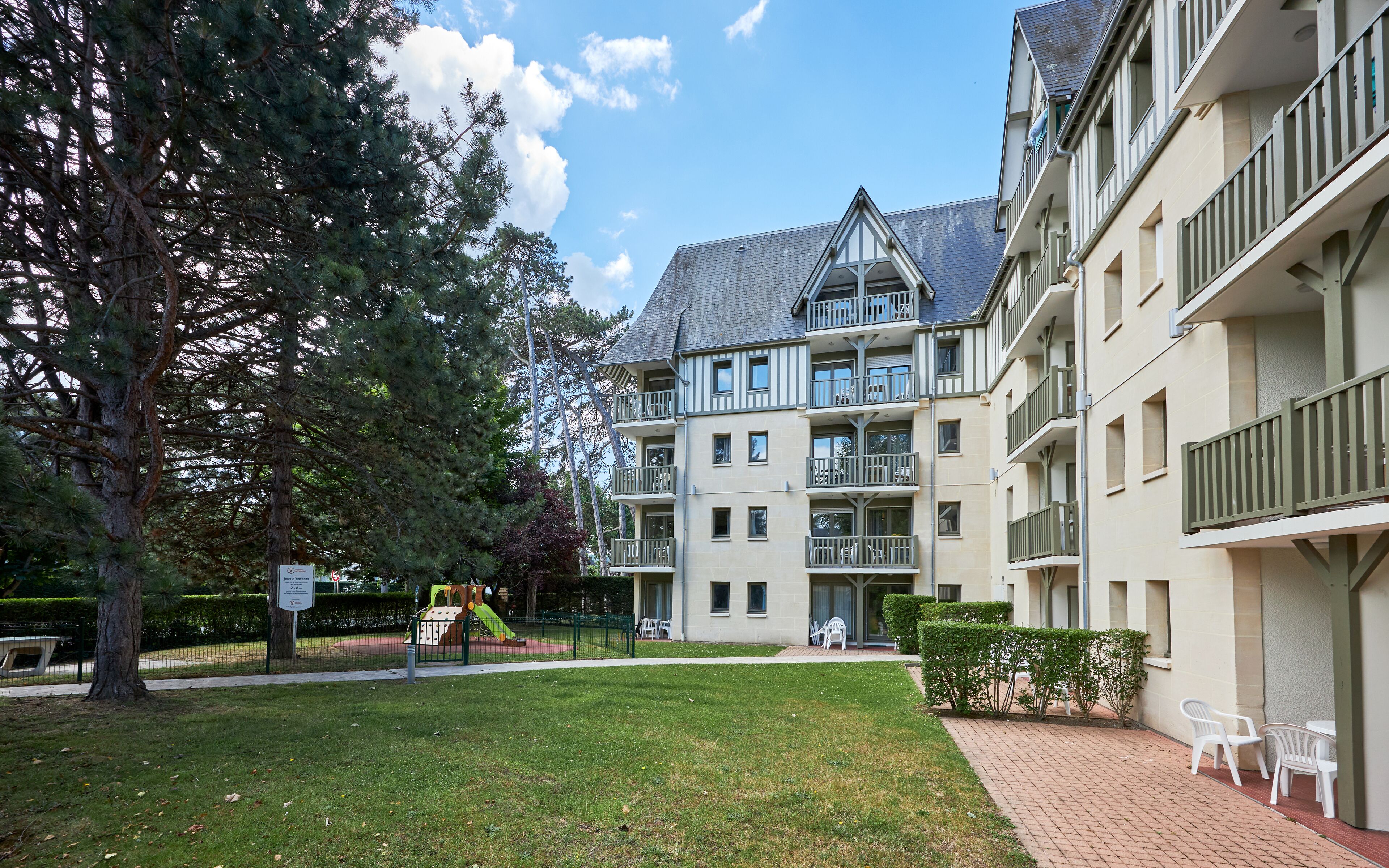 Un immeuble résidentiel à plusieurs étages, doté de balcons, d’une aire de jeux et d’un chemin en briques.