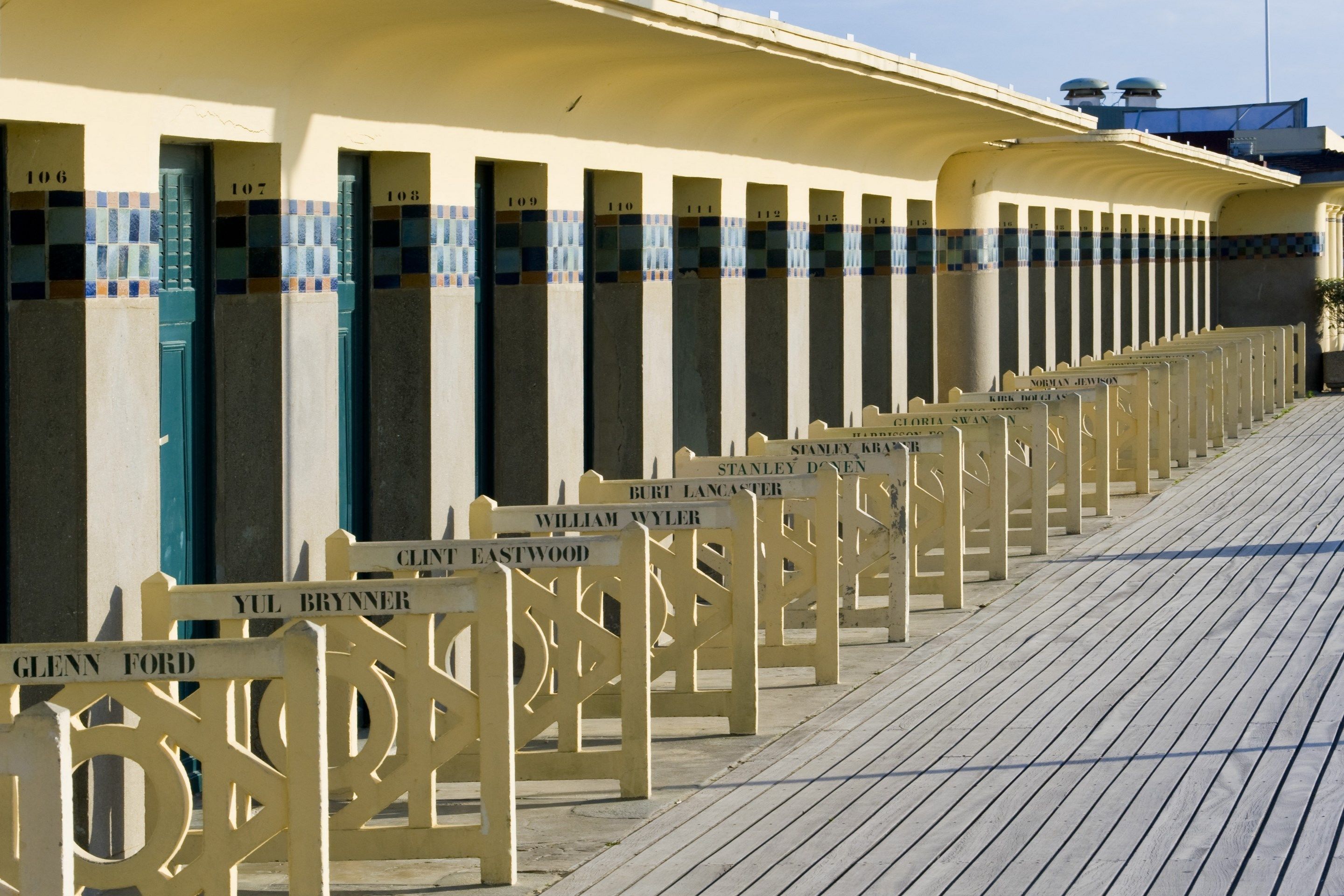 Une rangée de pierres tombales portant des noms, le long d’une promenade en bois.