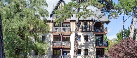 Un edificio de varios pisos con balcones, rodeado de árboles y vegetación.