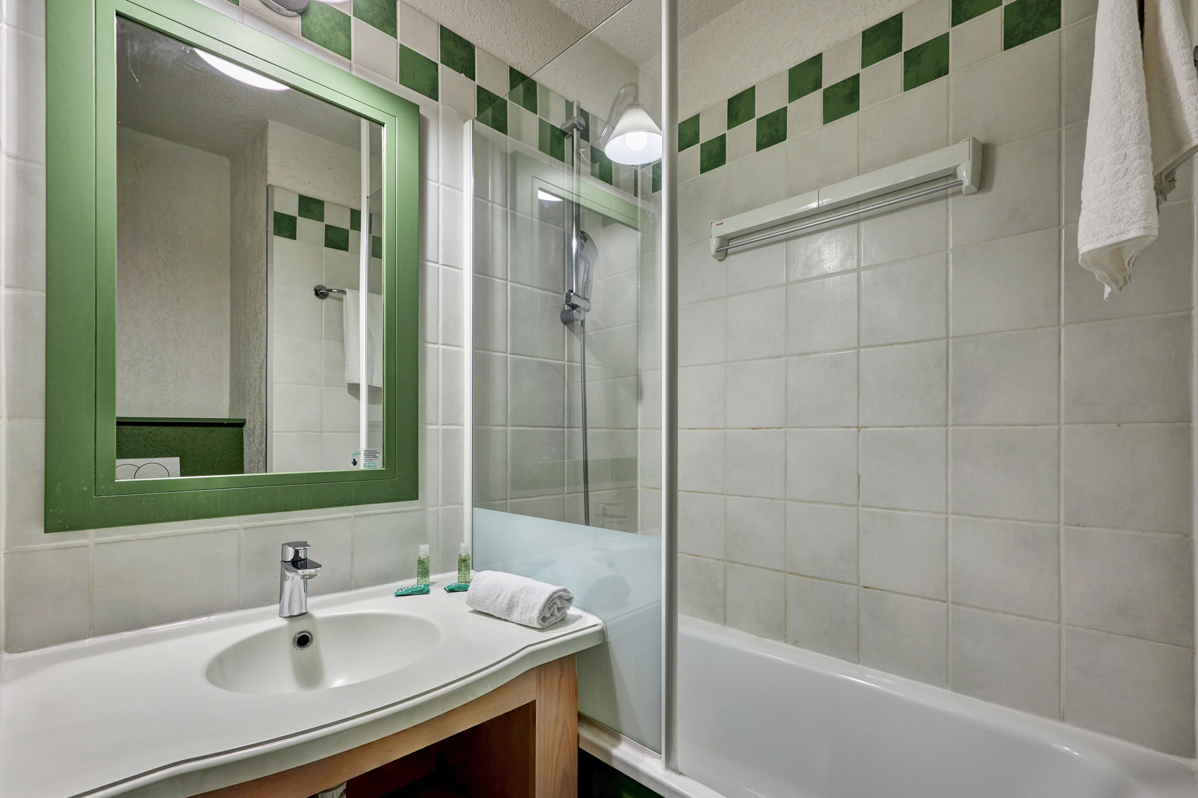 A bathroom with a sink, mirror, shower, and a towel rack.