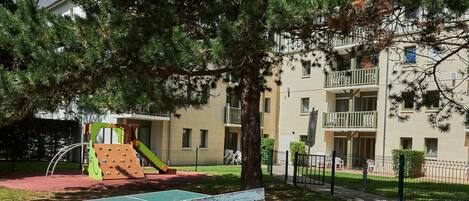 Una mesa de ping pong de hormigón en un área de parque con un parque infantil y edificios de apartamentos al fondo.