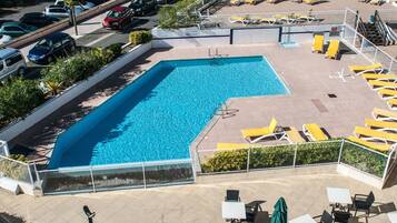 A swimming pool with yellow lounge chairs and a covered patio area.
