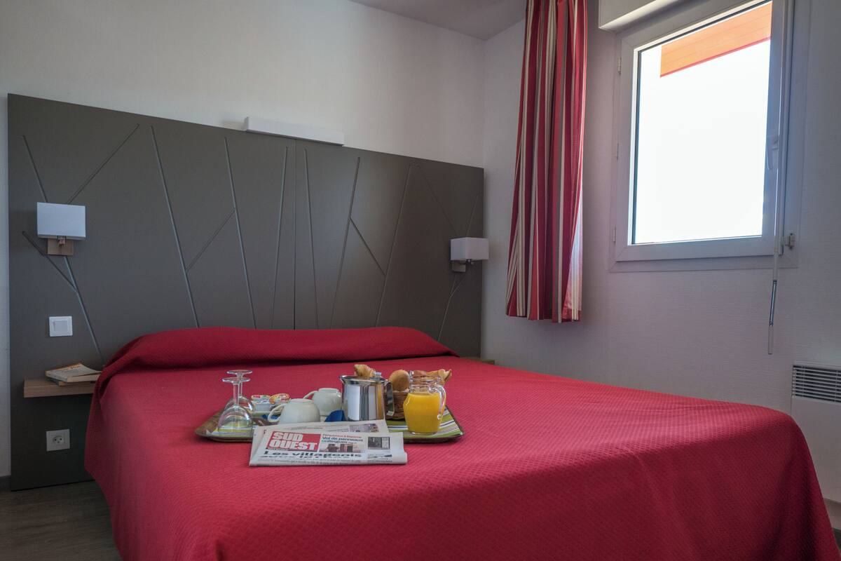 A hotel room with a bed, breakfast tray, and a window with curtains.