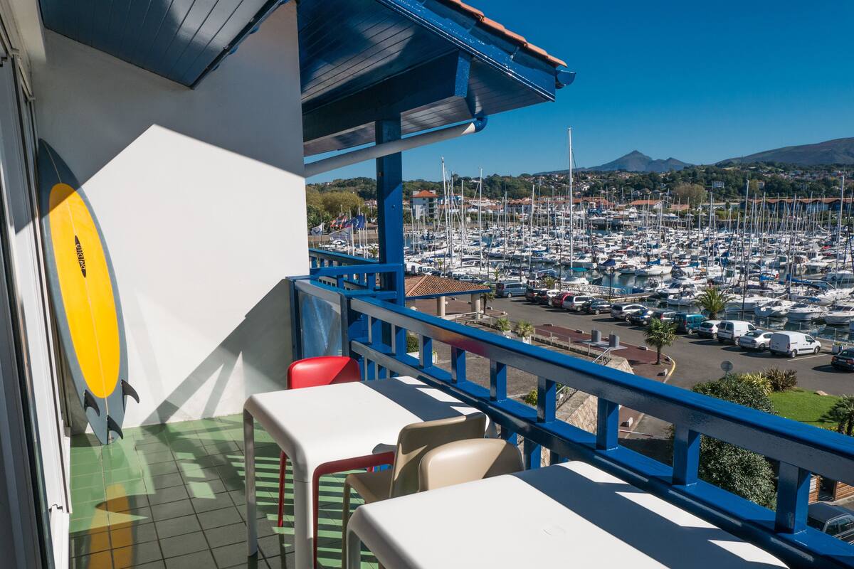A balcony with a view of a marina, chairs, and a surfboard.