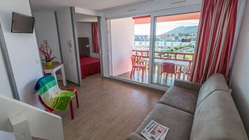Una habitación de hotel moderna con balcón, sofá, zona de comedor y una mesita con una planta.