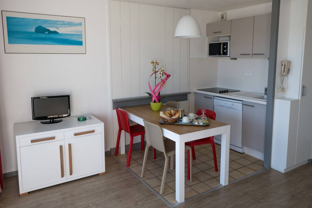 A compact kitchen with a dining area, white cabinets, a microwave, and a small refrigerator.