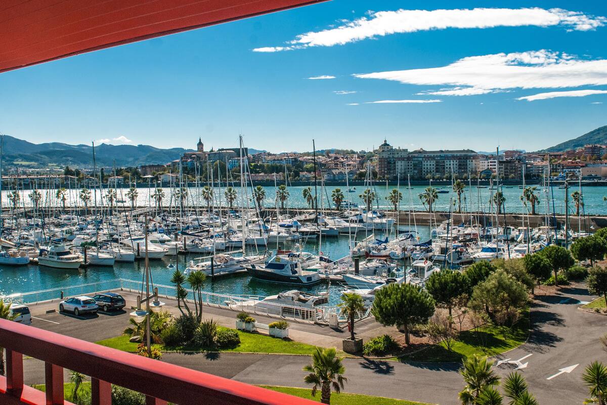 A marina with numerous boats docked, surrounded by buildings and palm trees.