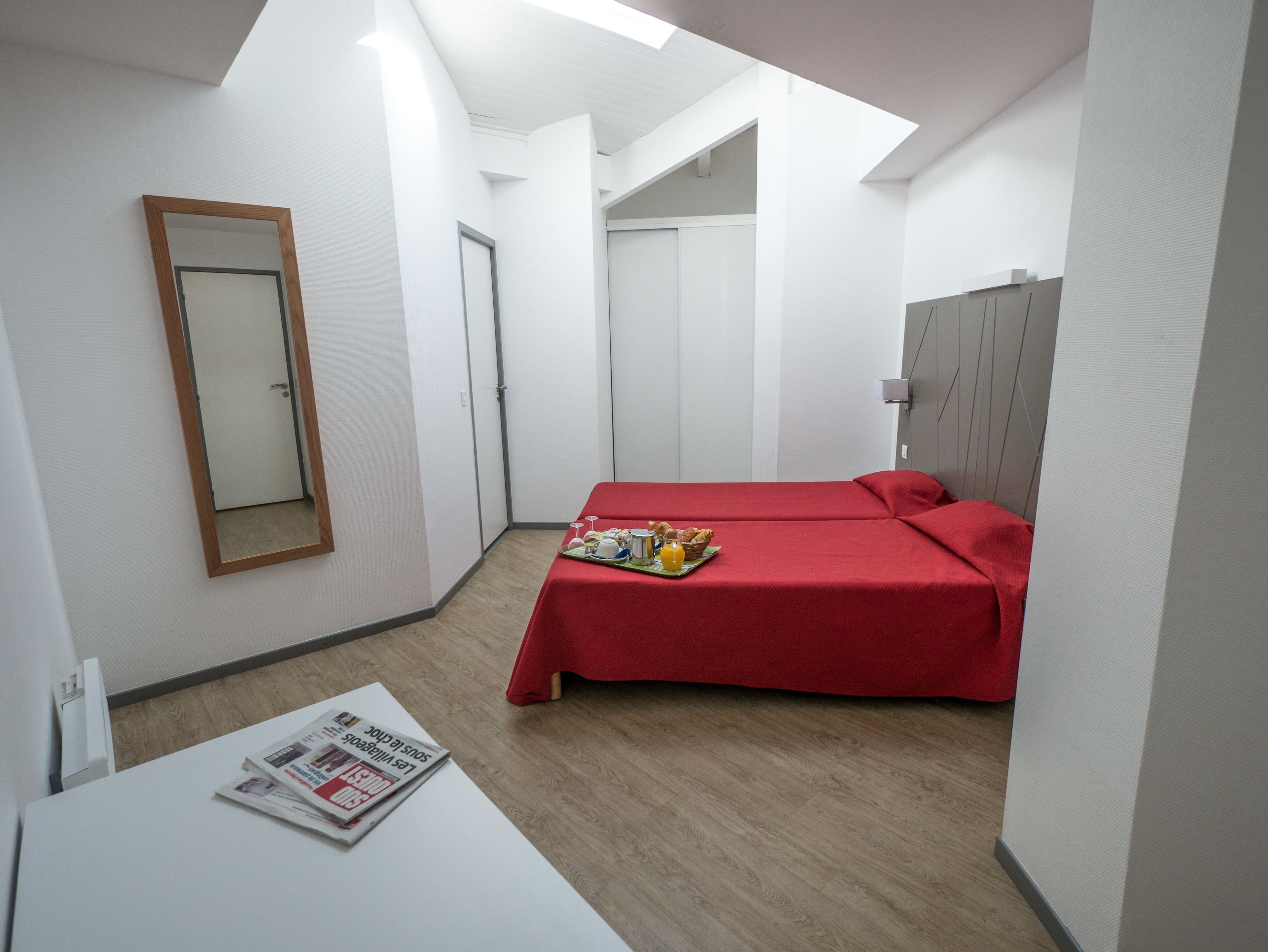 Een moderne hotelkamer met twee bedden, een klein tafeltje met een krant, en een spiegel aan de muur.