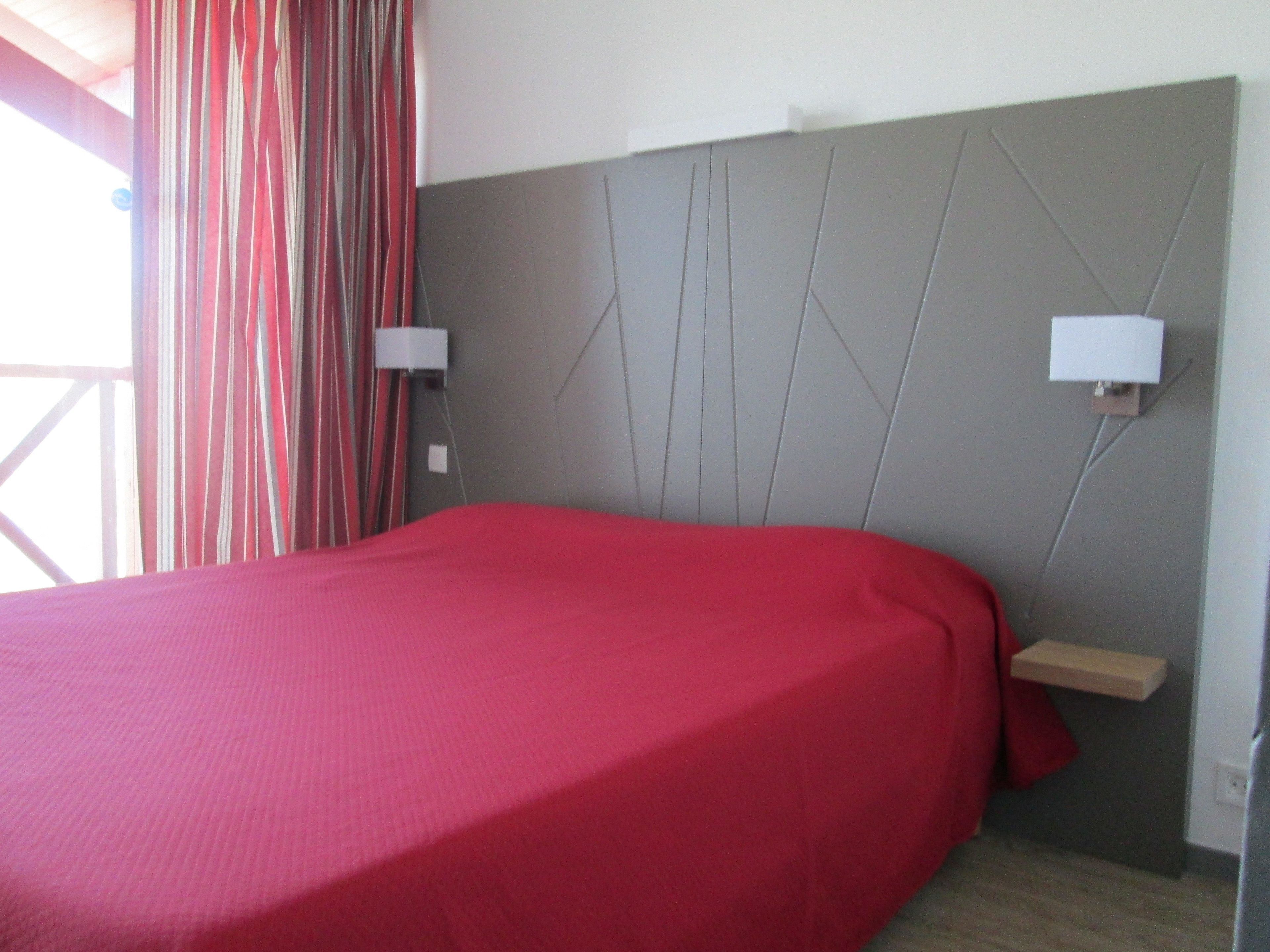 Una habitación de hotel con una cama, cabecera de diseño geométrico, dos lámparas de noche y una ventana con cortinas.