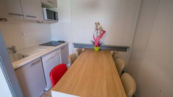 Una cocina compacta con microondas, lavamanos y lavavajillas pequeño. Hay una mesa de comedor de madera con cuatro sillas y un florero con flores.