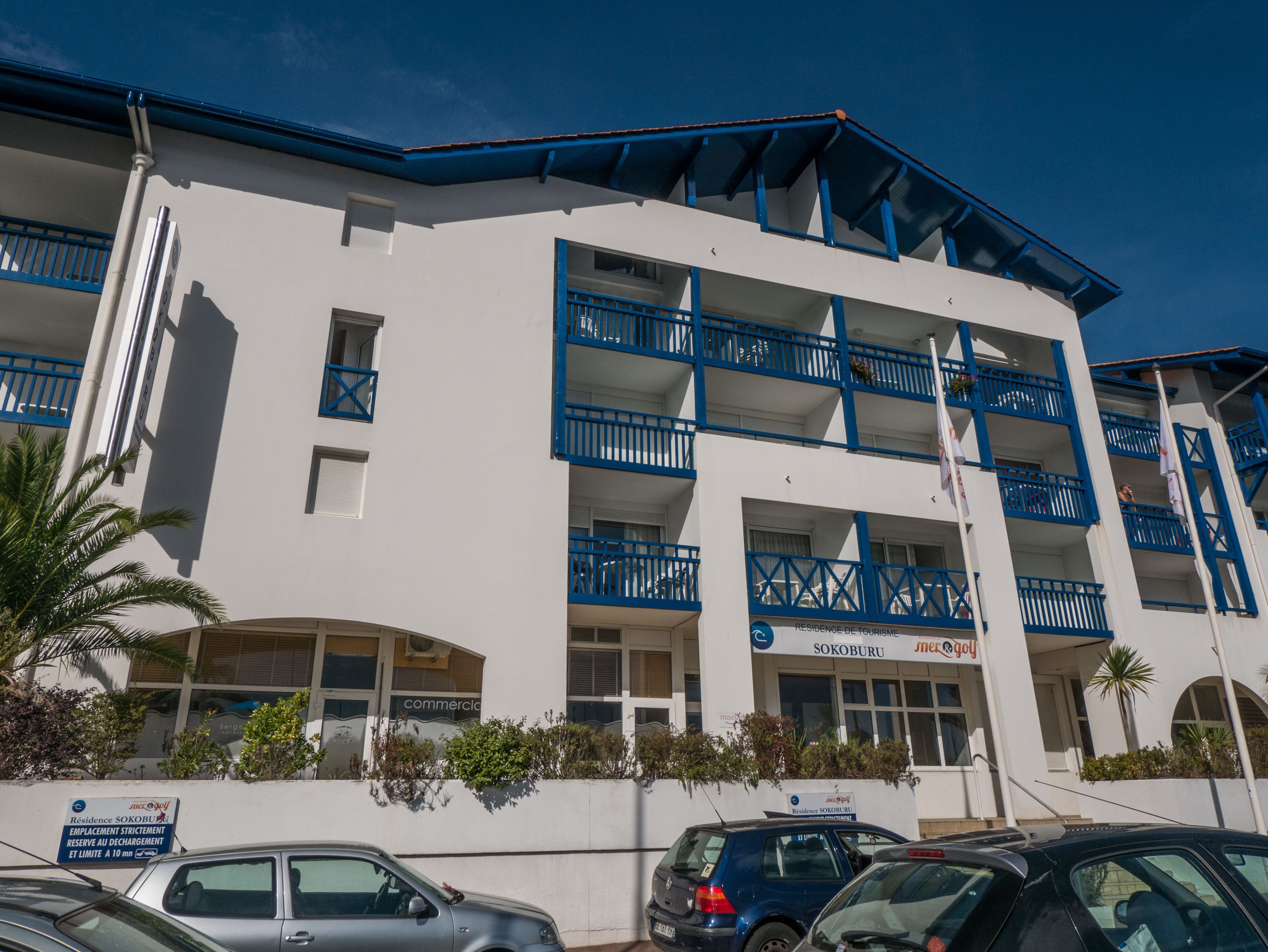 A multi-story hotel with blue balconies and a sign indicating it is a residence for tourism.