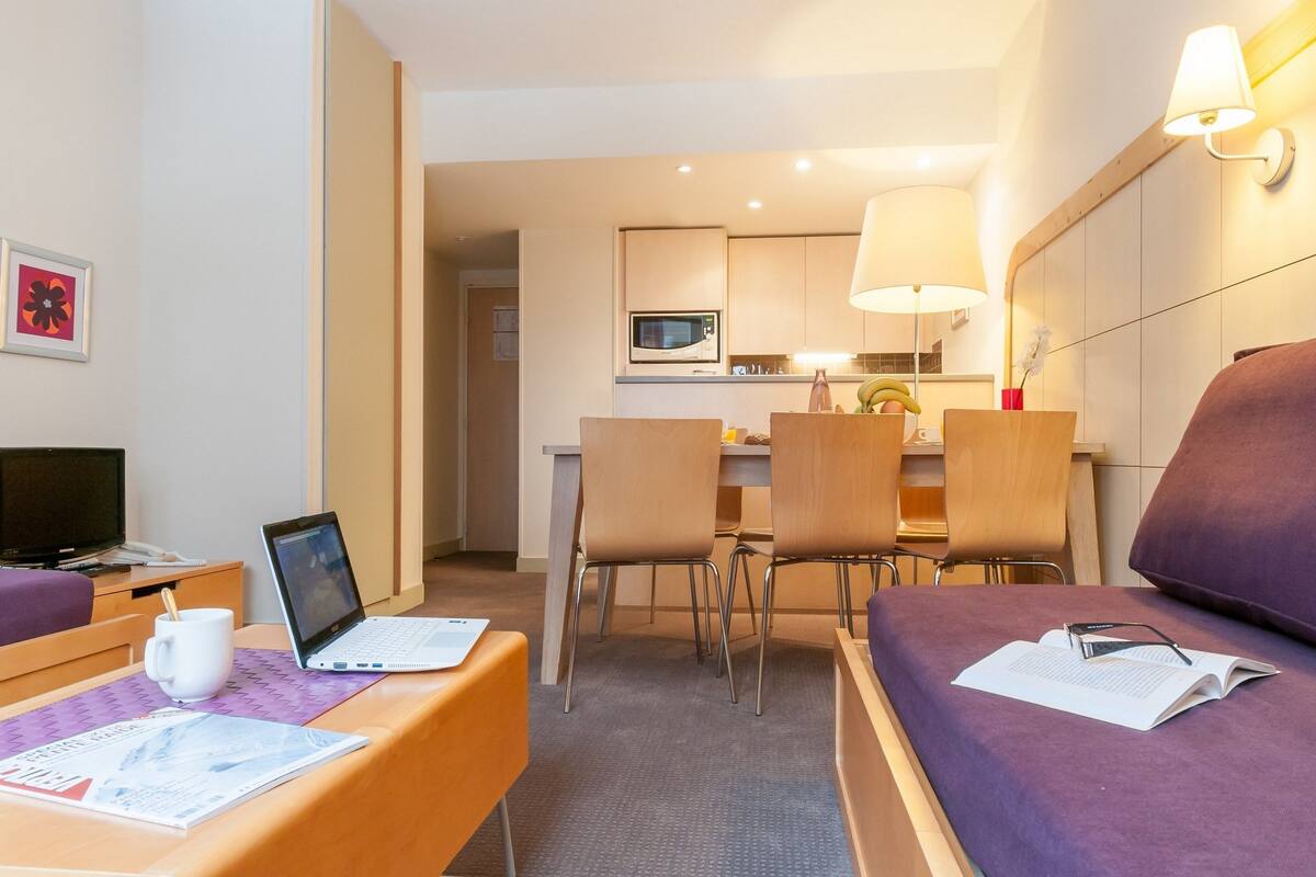 Ein Hotelzimmer mit Bett, Schreibtisch mit Laptop, Stuhl, Essbereich mit Tisch und Stühlen sowie einer Mikrowelle in der Küche.