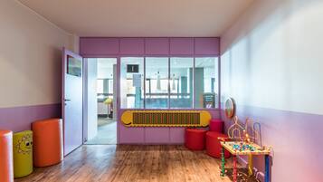Children can play and explore in this vibrant play area with a play table, stools, and a ball pit.