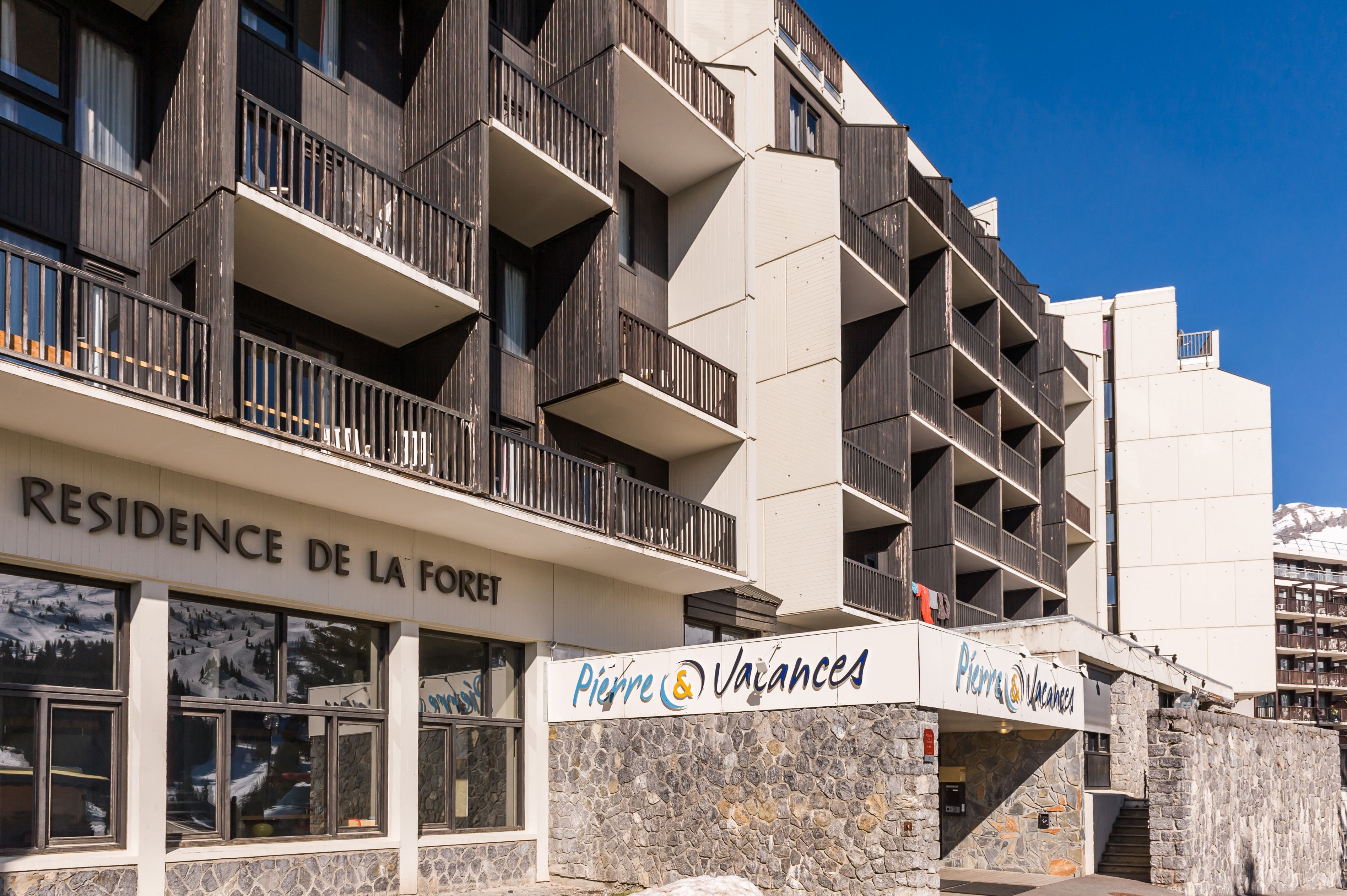 A multi-story building with balconies, a sign for "Residence de la Forêt," and another sign for "Pierre & Vacances."