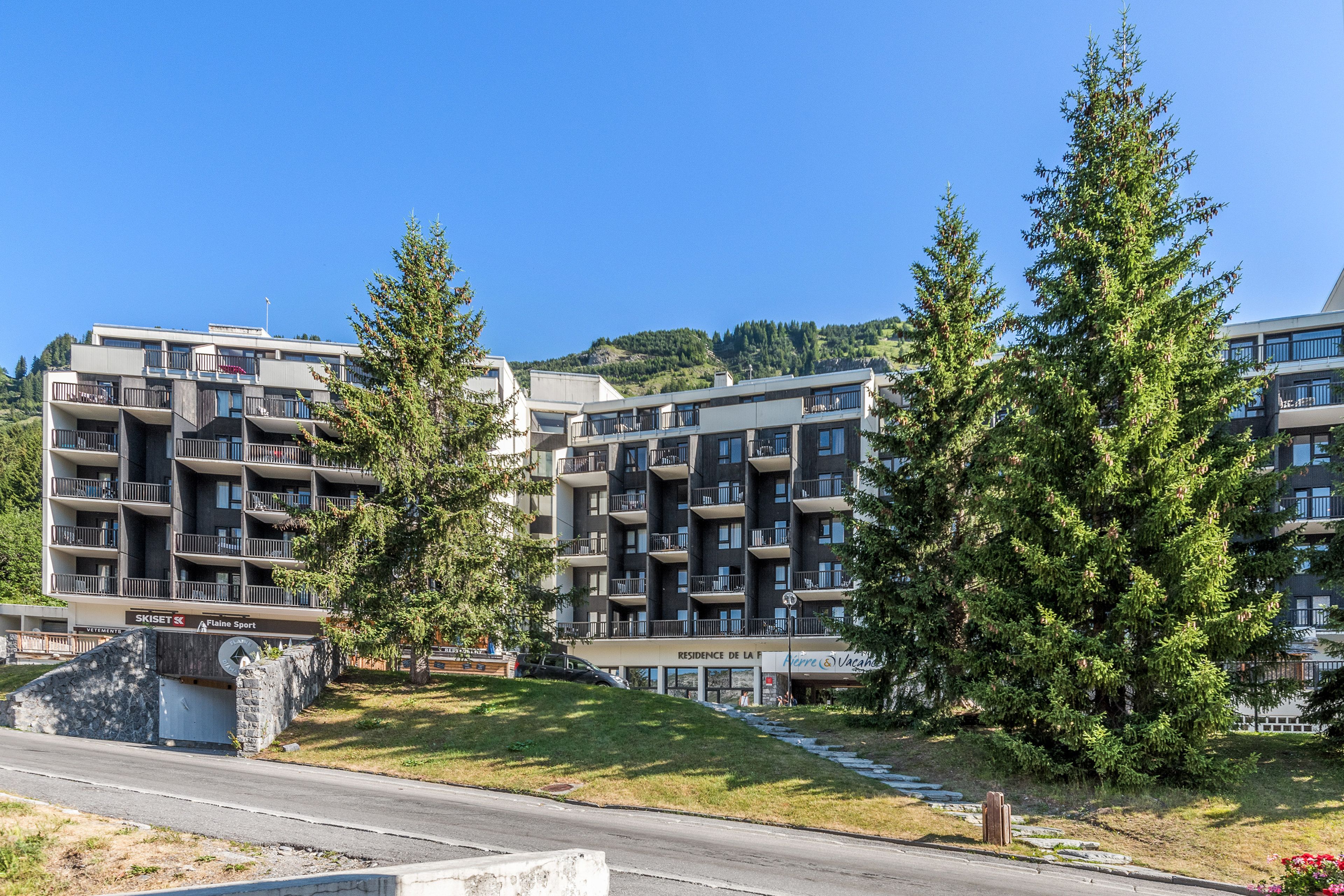 A multi-story residential building with balconies, a ski resort sign, and a nearby hotel.