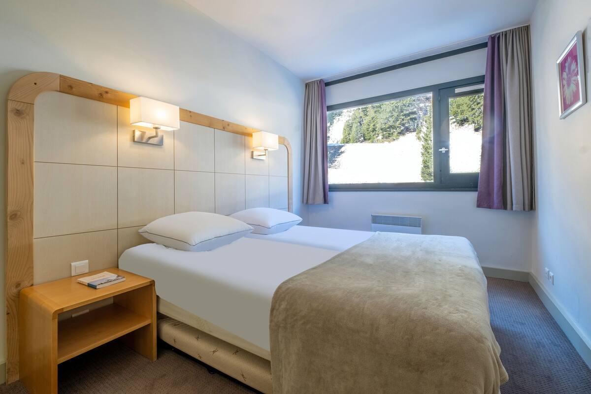 Ein Hotelzimmer mit einem großen Bett, zwei Nachttischlampen, einem Nachttisch und einem Fenster mit Vorhängen.