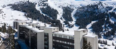 A multi-story building with a flat roof, surrounded by snow-covered mountains and trees.