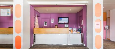 A reception area with a purple wall, a reception desk, and a television screen.