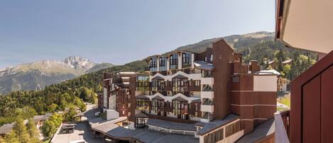 A multi-story hotel with a modern architectural design, featuring balconies and a parking area.