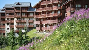 A multi-story hotel with balconies, surrounded by lush greenery and wildflowers. - Résidence Pierre & Vacances Les Valmonts (Les Belleville)