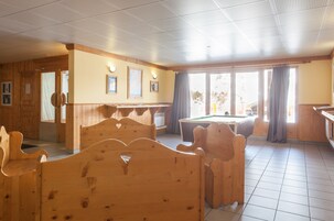 A room with wooden furniture, a pool table, and large windows.