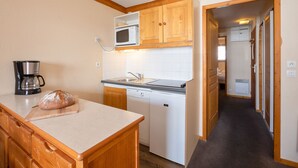 A compact kitchen with wooden cabinets, a microwave, a coffee maker, and a loaf of bread on the counter. - Résidence Pierre & Vacances Les Valmonts (Les Belleville)
