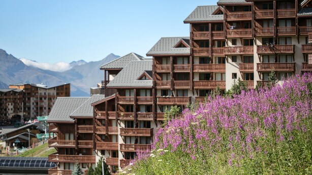 A hotel with multiple balconies, a mountainous backdrop, and a field of purple flowers in the foreground. - Résidence Pierre & Vacances Les Valmonts (Les Belleville)