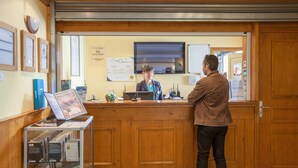 A reception desk with a wooden counter, a computer, and informational posters on the wall. - Résidence Pierre & Vacances Les Valmonts (Les Belleville)