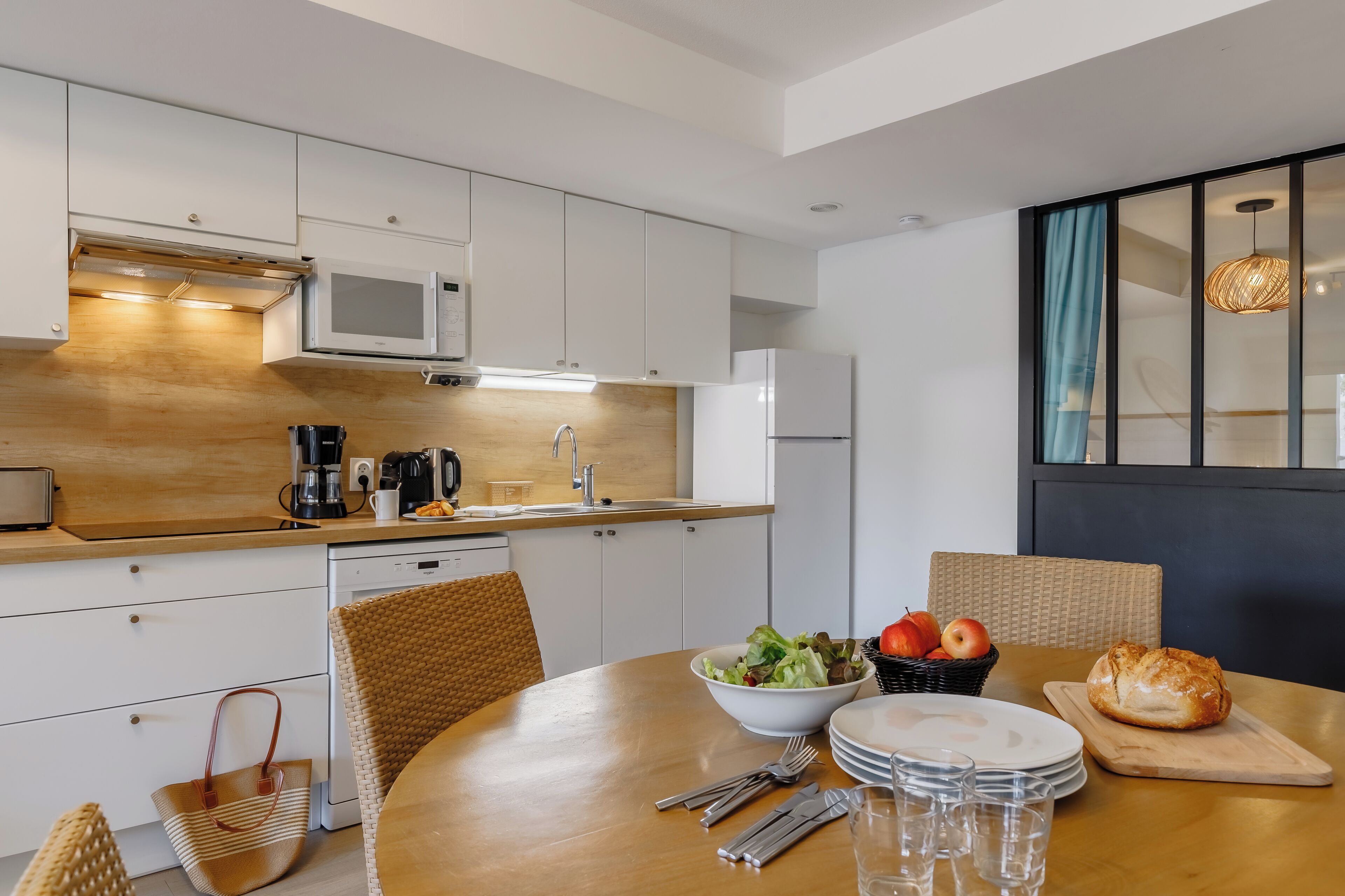 A modern kitchen with white cabinets, a wooden countertop, and a dining area with a table set for two.
