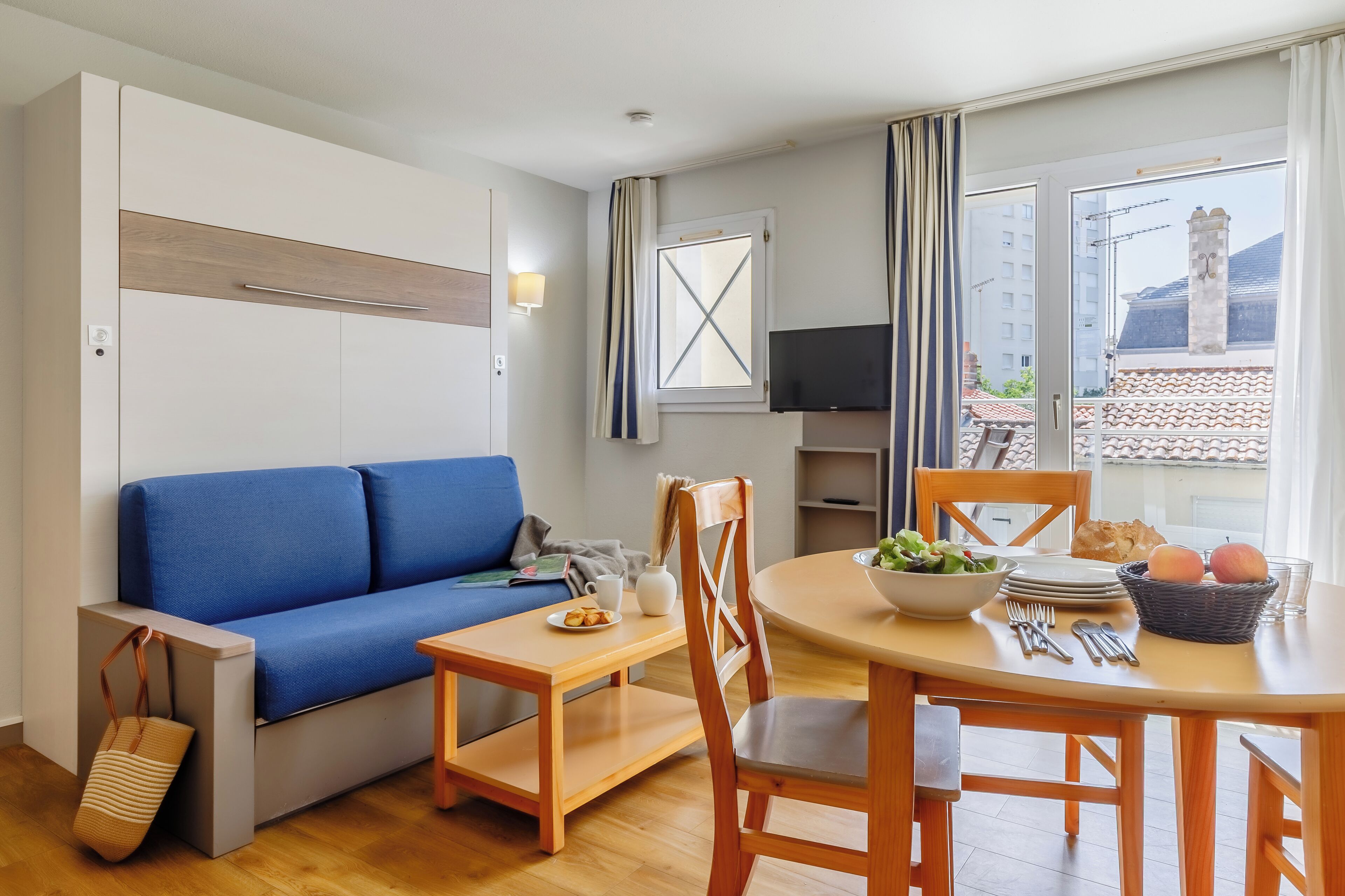 A modern living room with a blue sofa, wooden dining table, and chairs.