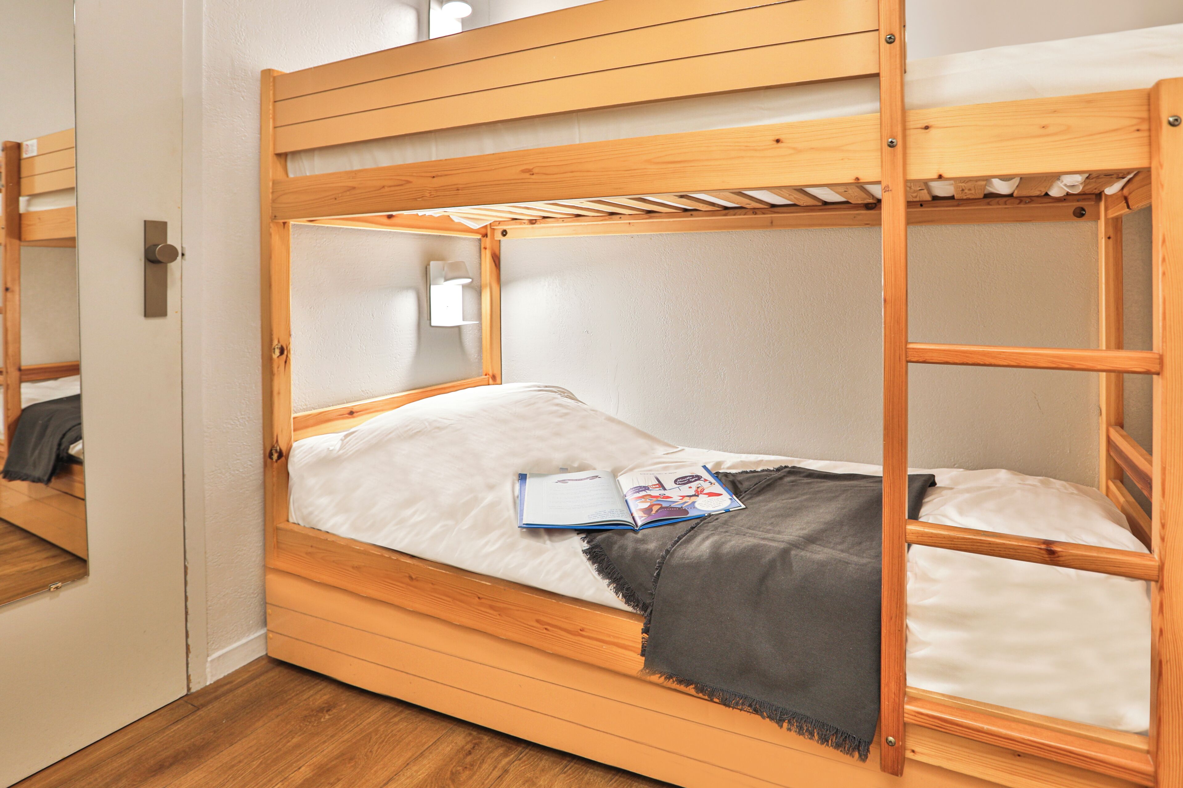 Ein Stockbett mit Holzbettrahmen, weißer Bettwäsche und einer Zeitschrift auf der Matratze.