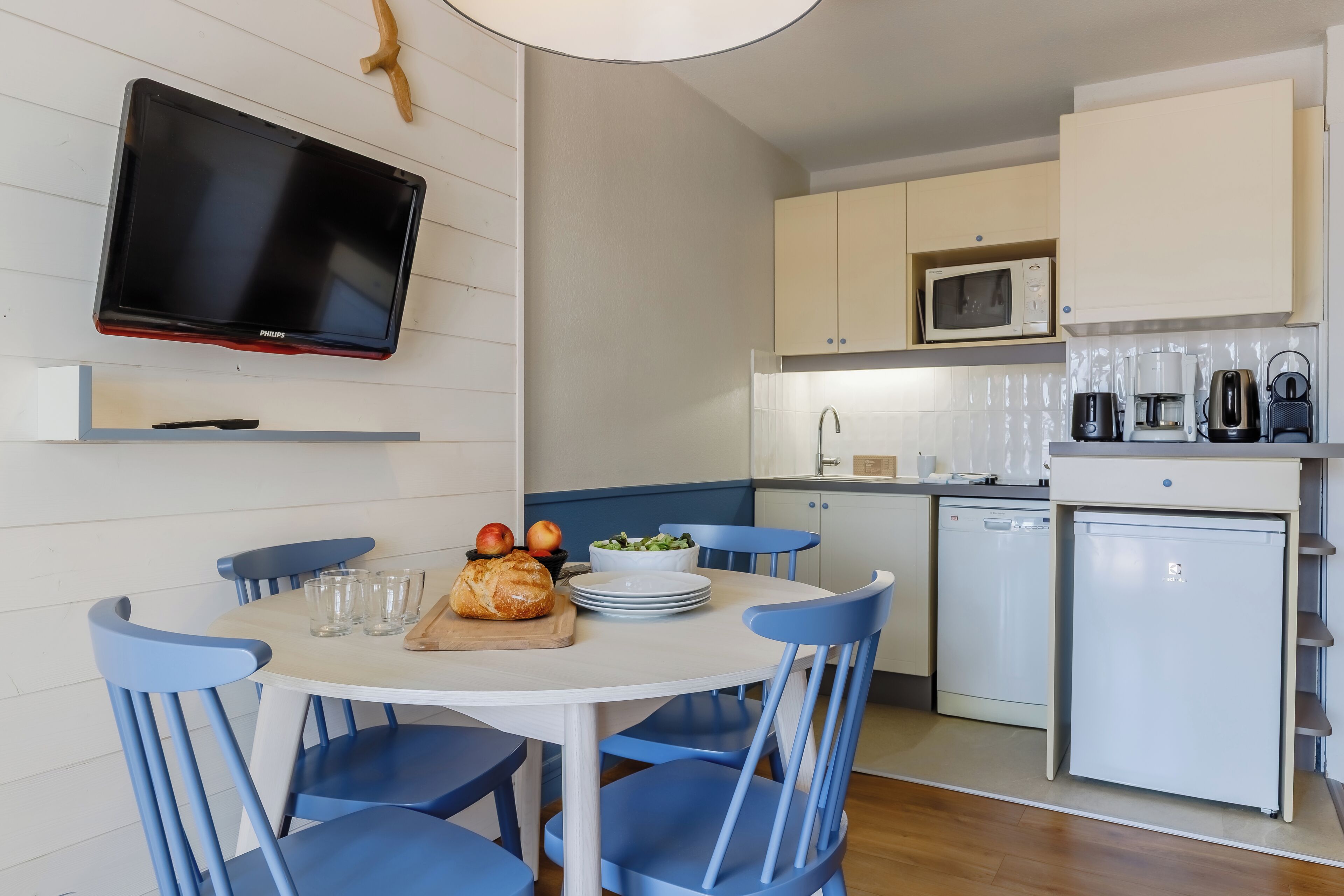 A compact kitchen with a dining area, white cabinets, a microwave, a coffee maker, and a small refrigerator.