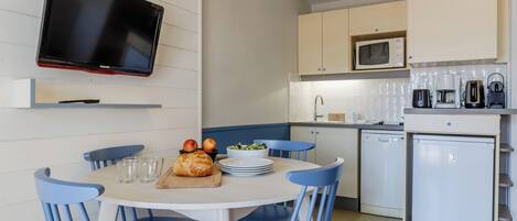 A compact kitchen with a dining area, white cabinets, a microwave, a coffee maker, and a small refrigerator.