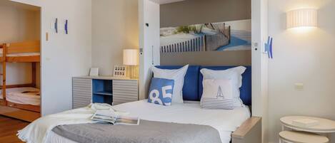 A bedroom with a bunk bed, a bedside table, a lamp, and a wall-mounted artwork.