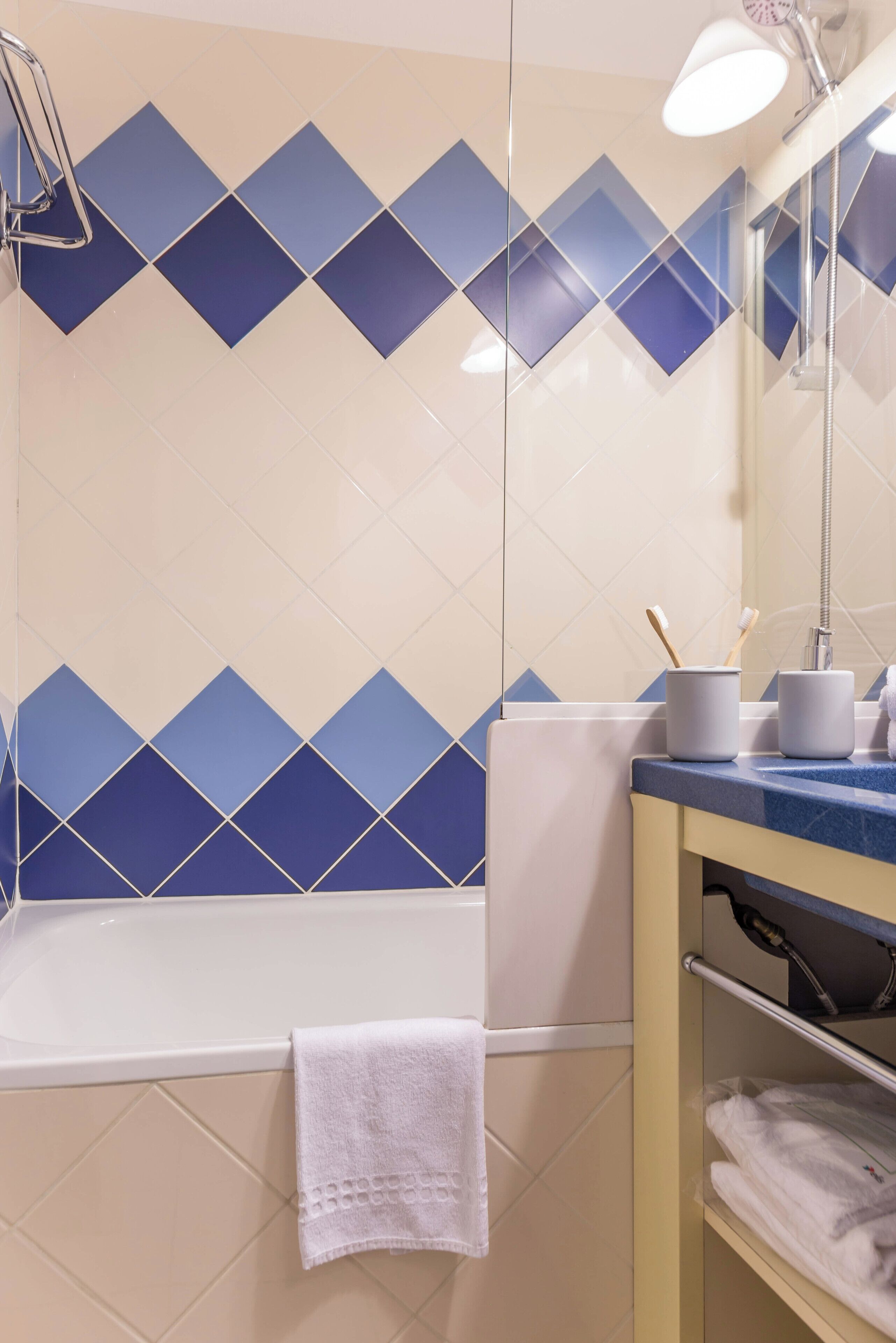 Ein Badezimmer mit blauen und weißen Fliesen, einer weißen Badewanne, einem Handtuch auf dem Boden und einem Ablagefach mit Handtüchern und Toilettenartikeln.