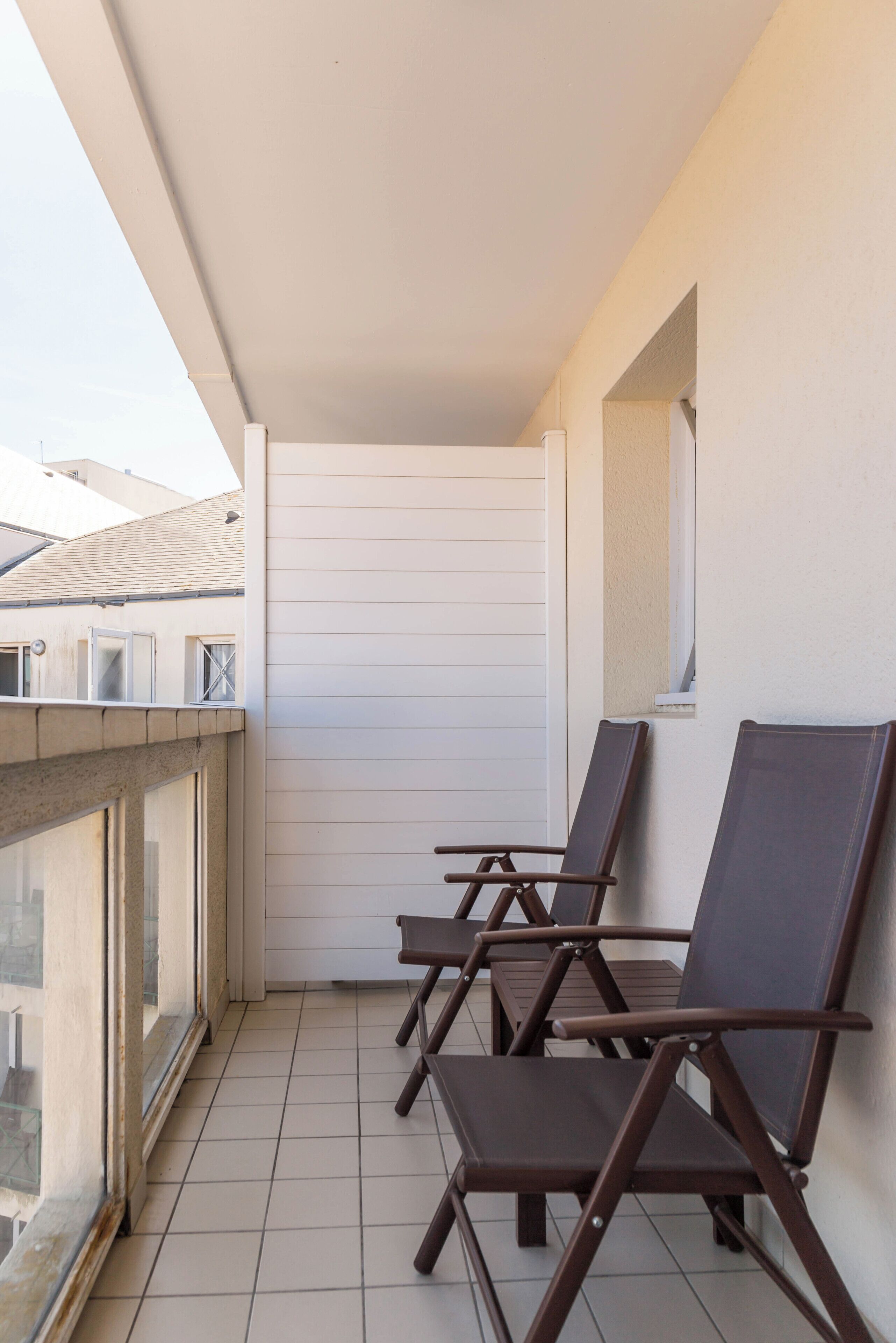 A balcony with four brown chairs, a white wall, and a window.