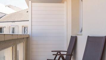 A balcony with four brown chairs, a white wall, and a window.