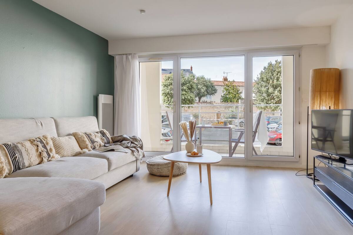 Un salon comprenant un canapé, une table ronde, un téléviseur et un balcon donnant sur l’extérieur.
