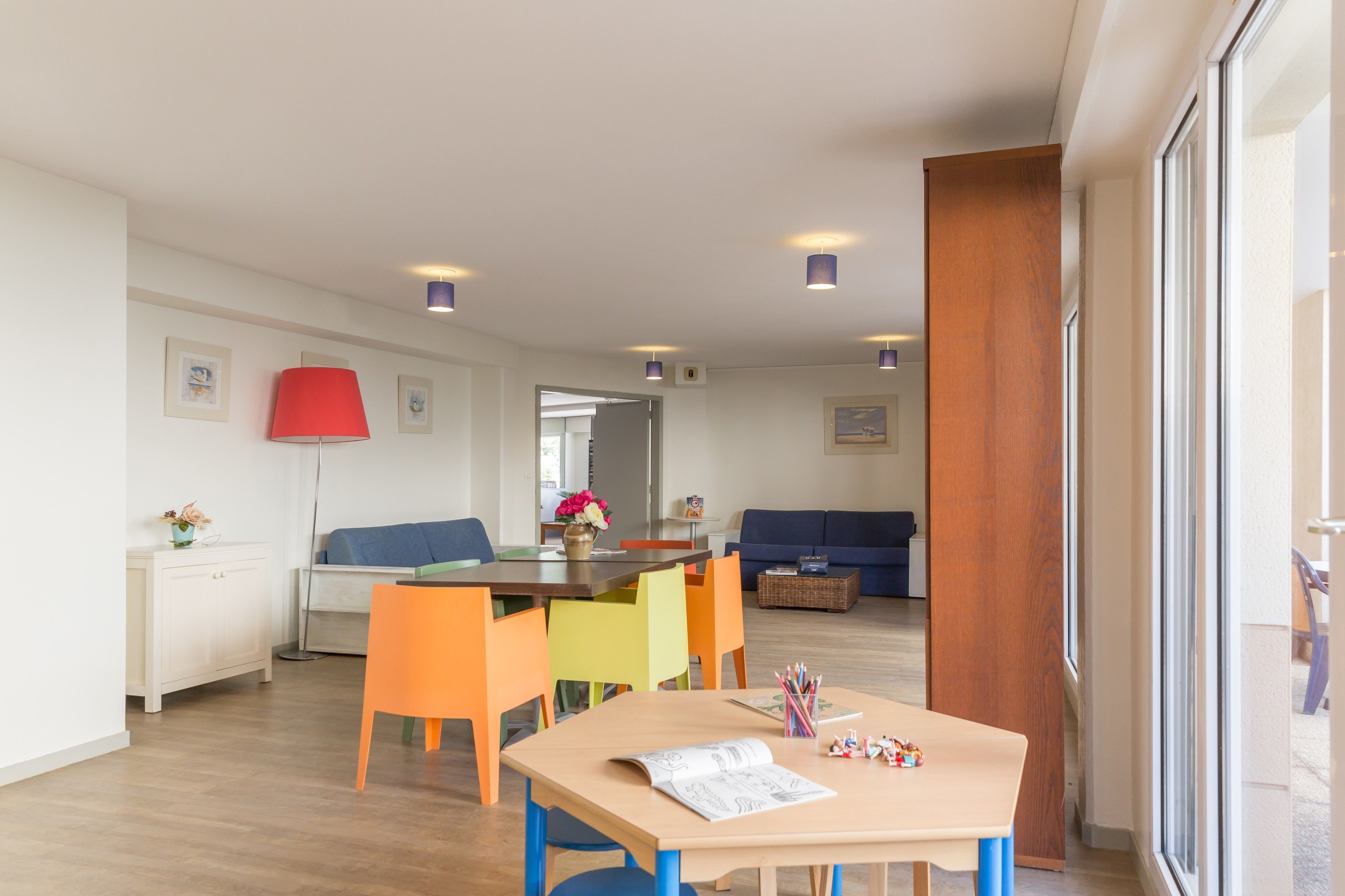 Una sala de estar moderna con piso de madera, una mesa de comedor con sillas coloridas, un sofá azul y una lámpara roja.