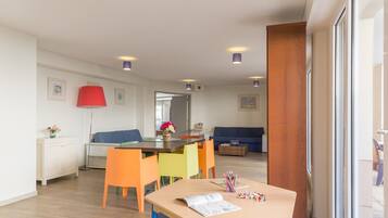 Una sala de estar moderna con piso de madera, una mesa de comedor con sillas coloridas, un sofá azul y una lámpara roja.