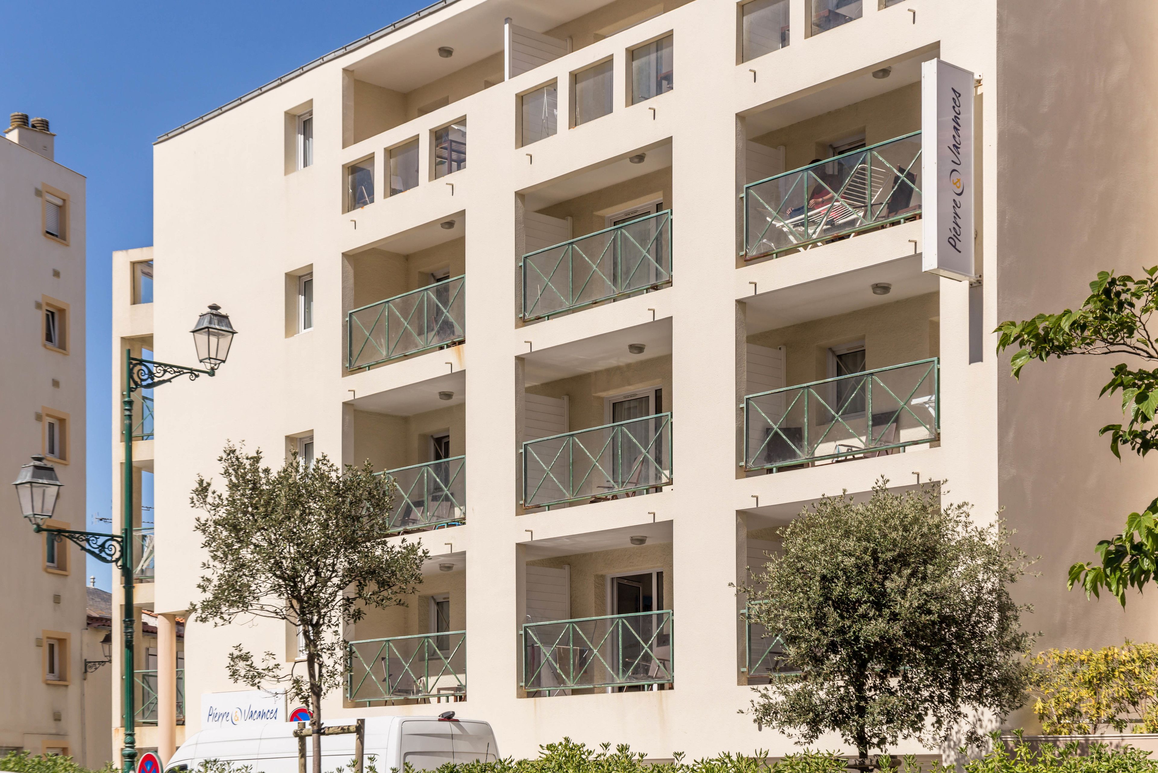 A multi-story building with balconies, a sign for "Pierre Vacances," and a street lamp.