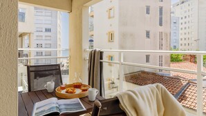Un balcón con una mesa dispuesta para el desayuno, un libro y vistas a edificios.