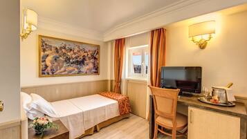 Une chambre d’hôtel avec un lit, un bureau avec une télévision, une chaise, une fenêtre avec des rideaux et un tableau au mur.