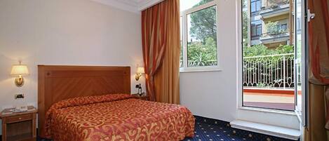 A hotel room with a large bed, a nightstand, a lamp, a window with curtains, and a balcony with a railing.