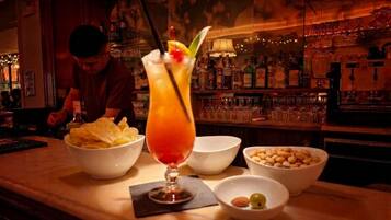 A bar setting with a cocktail, bowls of snacks, and a bartender preparing drinks.