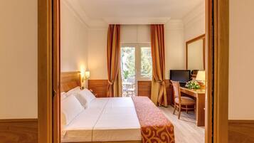 Habitación de hotel con cama, escritorio, silla, televisor y ventana con cortinas.