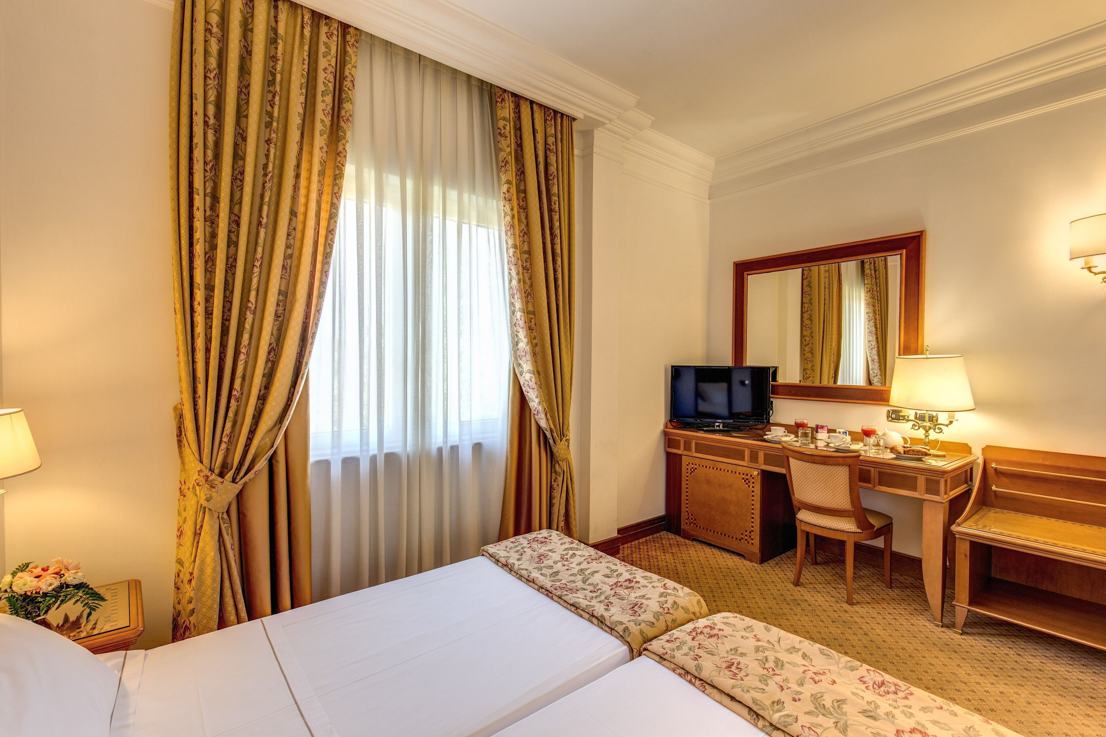 A hotel room with a bed, a desk with a computer, a chair, and a television.