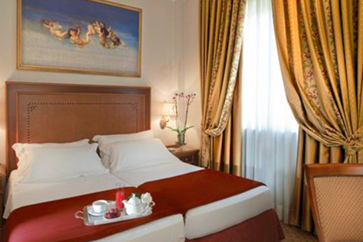 A hotel room with a large bed, a nightstand, a lamp, a painting on the wall, and curtains.